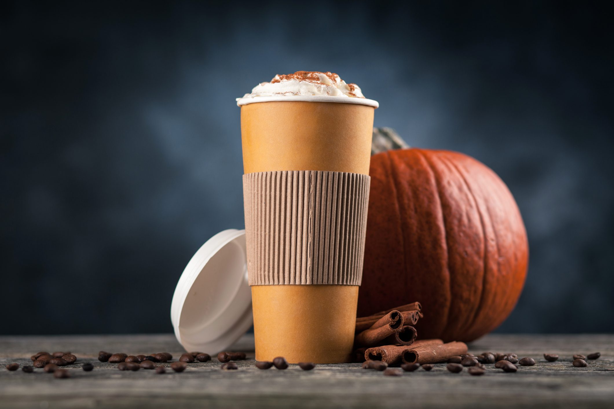Pumpkin spice latte in a paper cup on dark background in front of a pumpkin